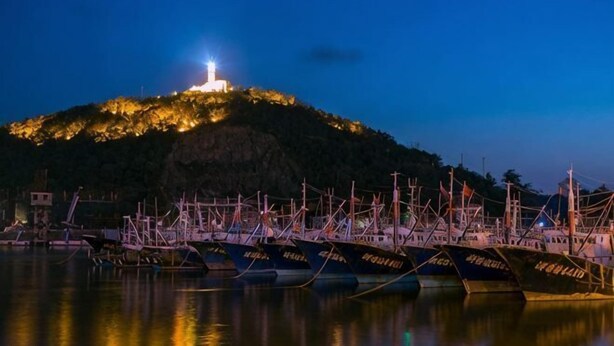 A harbor at dusk with boats docked, a hill with a light, and calm water reflecting the scene. - Zhoushan Shenjiamen Zhongjing Hotel(Banshengdong Passenger Terminal Branch) (Zhoushan)