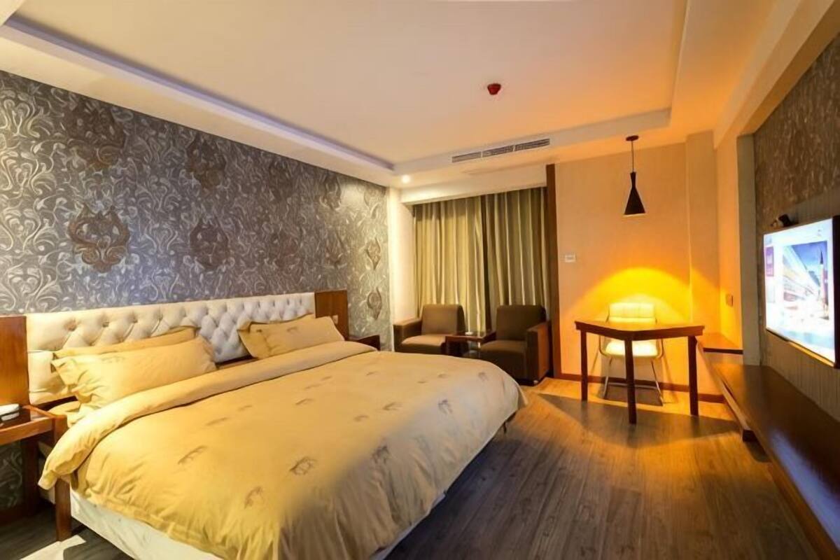 A hotel room with a large bed, a desk, two chairs, a TV, and a patterned wall.