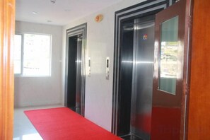 An elevator area with a red carpet, two elevators, and a door with a number sign. - Zhoushan Shenjiamen Zhongjing Hotel(Banshengdong Passenger Terminal Branch) (Zhoushan)