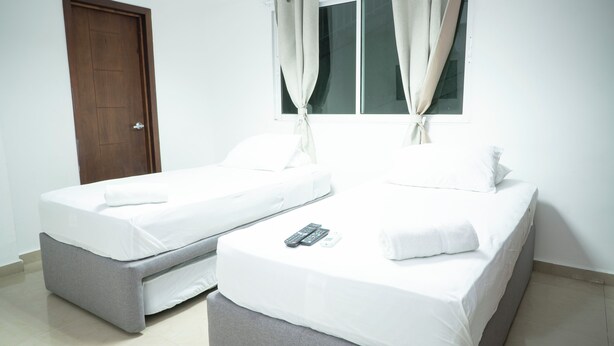 A room with two single beds, a window with curtains, a door, and a remote control on one bed. - 2-bedroom apartment in Bocagrande- Cartagena (Bolívar)