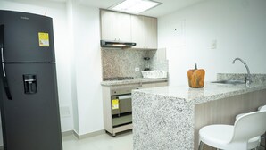 A kitchen with a black refrigerator, a built-in stove, a microwave, and a sink. There are white bar stools and a decorative pumpkin on the counter. - 2-bedroom apartment in Bocagrande- Cartagena (Bolívar)