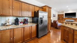 Eine moderne Küche mit Holzausstattung, einem Edelstahlkühlschrank und einem eingebauten Backofen. Auf der Arbeitsfläche stehen eine Kaffeemaschine und eine Mikrowelle.