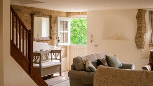 A cozy living room with a staircase, a wooden chair, a sofa, and a window with a view of greenery. - Pickett Cottage - Pet friendly near Northleach (Northleach)