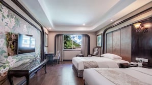 A hotel room with two beds, a TV, a desk, and a window with a view of greenery. - Jiuyuan Hotel (Jiuzhaigou)