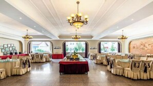 A spacious banquet hall with multiple round tables, each with chairs, and a central table with a red tablecloth. - Jiuyuan Hotel (Jiuzhaigou)