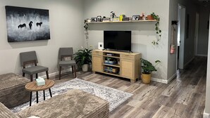 Een moderne woonkamer met een flatscreen televisie, comfortabele zithoek, een plafondventilator en een boekenkast met decoratieve objecten.