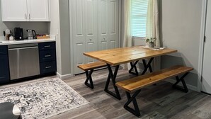 Een kleine keuken met een houten tafel en bankje, een koffiezetapparaat en een potplant.