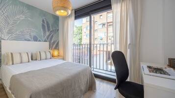 Une chambre à coucher comprenant un lit, un bureau, une chaise, une grande fenêtre avec des rideaux et une fresque murale.