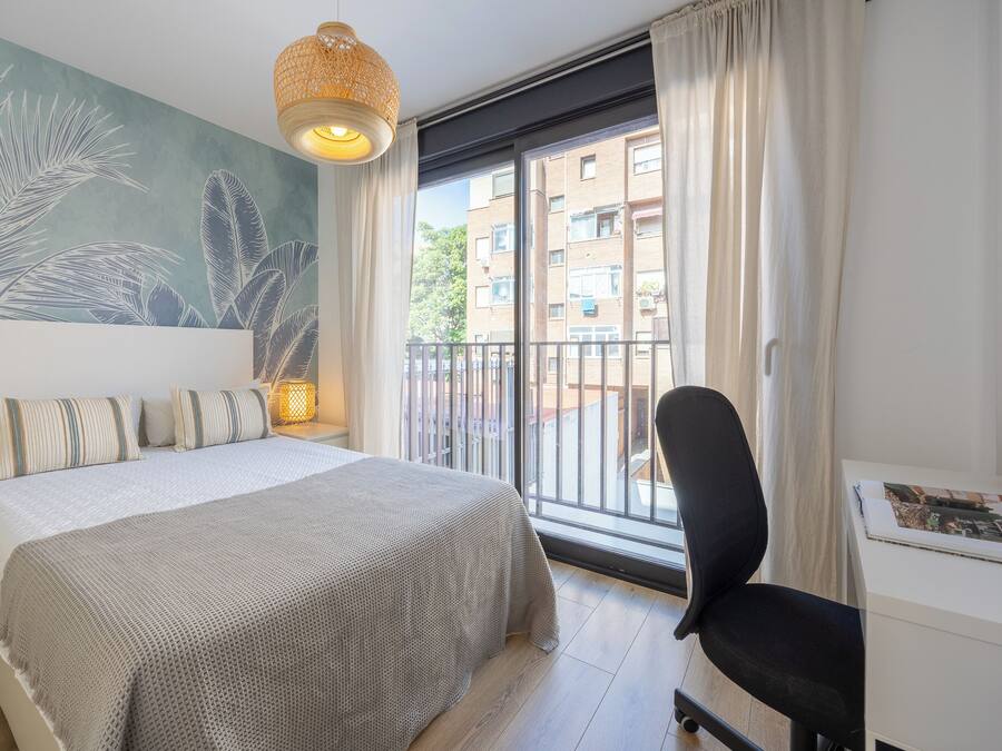 Une chambre à coucher comprenant un lit, un bureau, une chaise, une grande fenêtre avec des rideaux et une fresque murale.