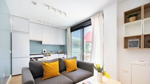 A modern apartment with a grey sofa, a dining table, a kitchen area, and a view of the outside. - Edmond Vibes Airport - Ifema Hub (Madrid)