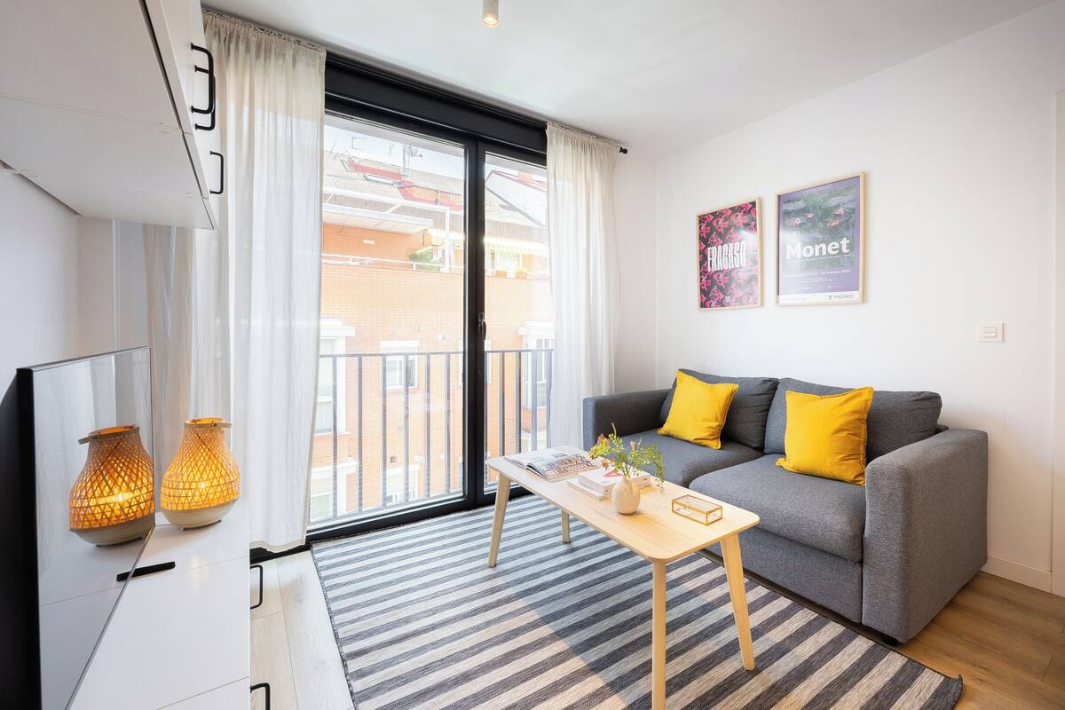 Una sala de estar moderna con un sofá gris, cojines amarillos, una mesa de centro de madera y dos lámparas decorativas.