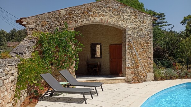A stone building with a pool, two lounge chairs, and a wooden door.