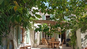 A covered outdoor seating area with a table and chairs, surrounded by potted plants and a stone wall.