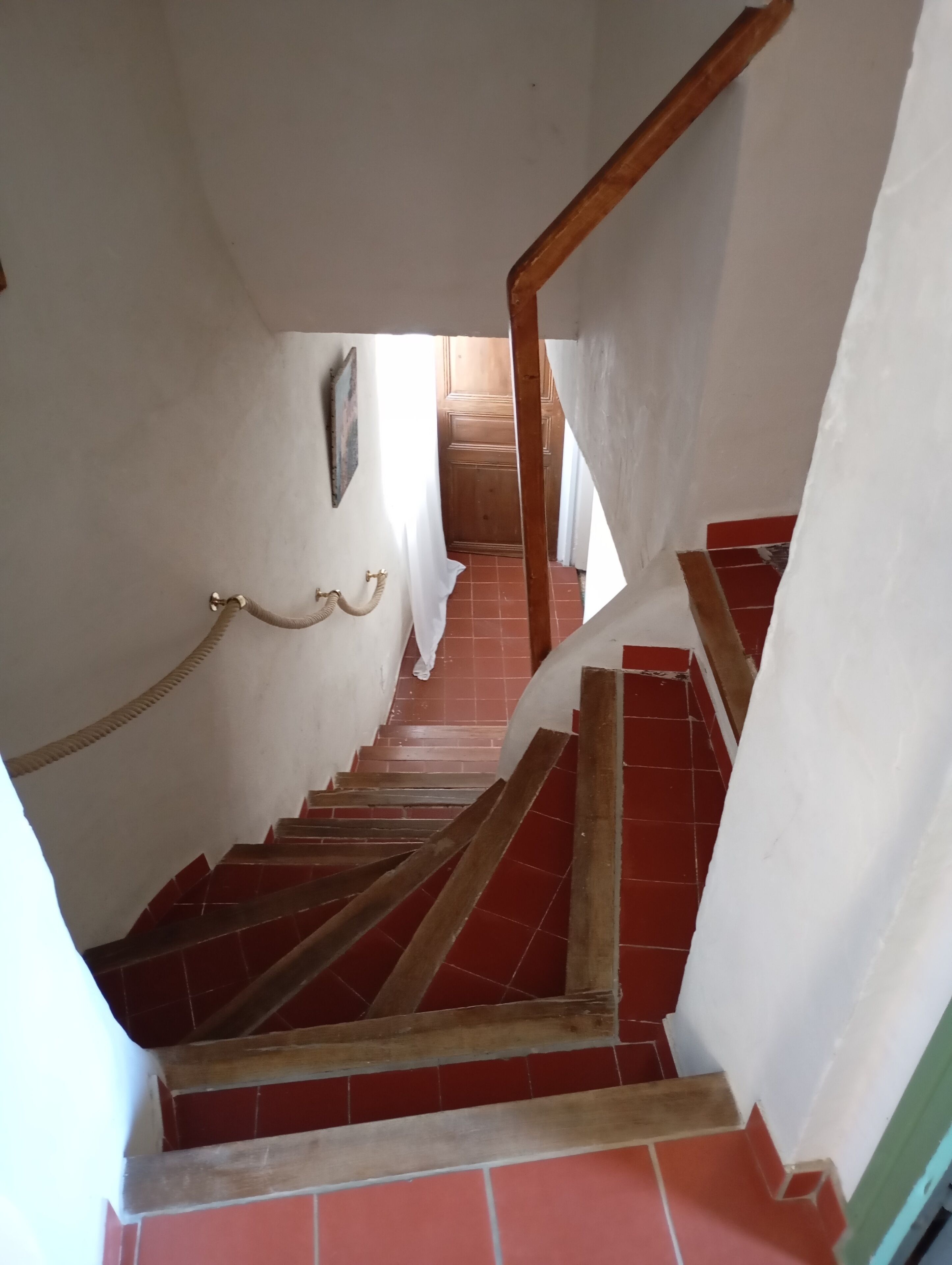 A staircase with red-tiled steps and wooden handrails, leading to a door at the top.