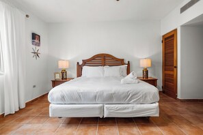 Una cama doble bien hecha con ropa de cama blanca, dos mesitas de noche con lámparas, una decoración de estrella en la pared y una puerta de madera.
