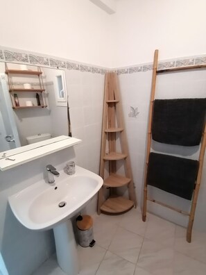 Un baño con lavamanos, espejo y estantes blancos.