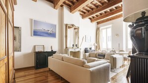 A spacious living room with a wooden ceiling, a large sofa, a fireplace, and a dining area. - Charming Apartment in the Heart of Florence (Firenze)