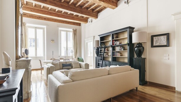 A spacious living room with a large beige sofa, wooden flooring, a bookshelf, and a lamp. - Charming Apartment in the Heart of Florence (Firenze)