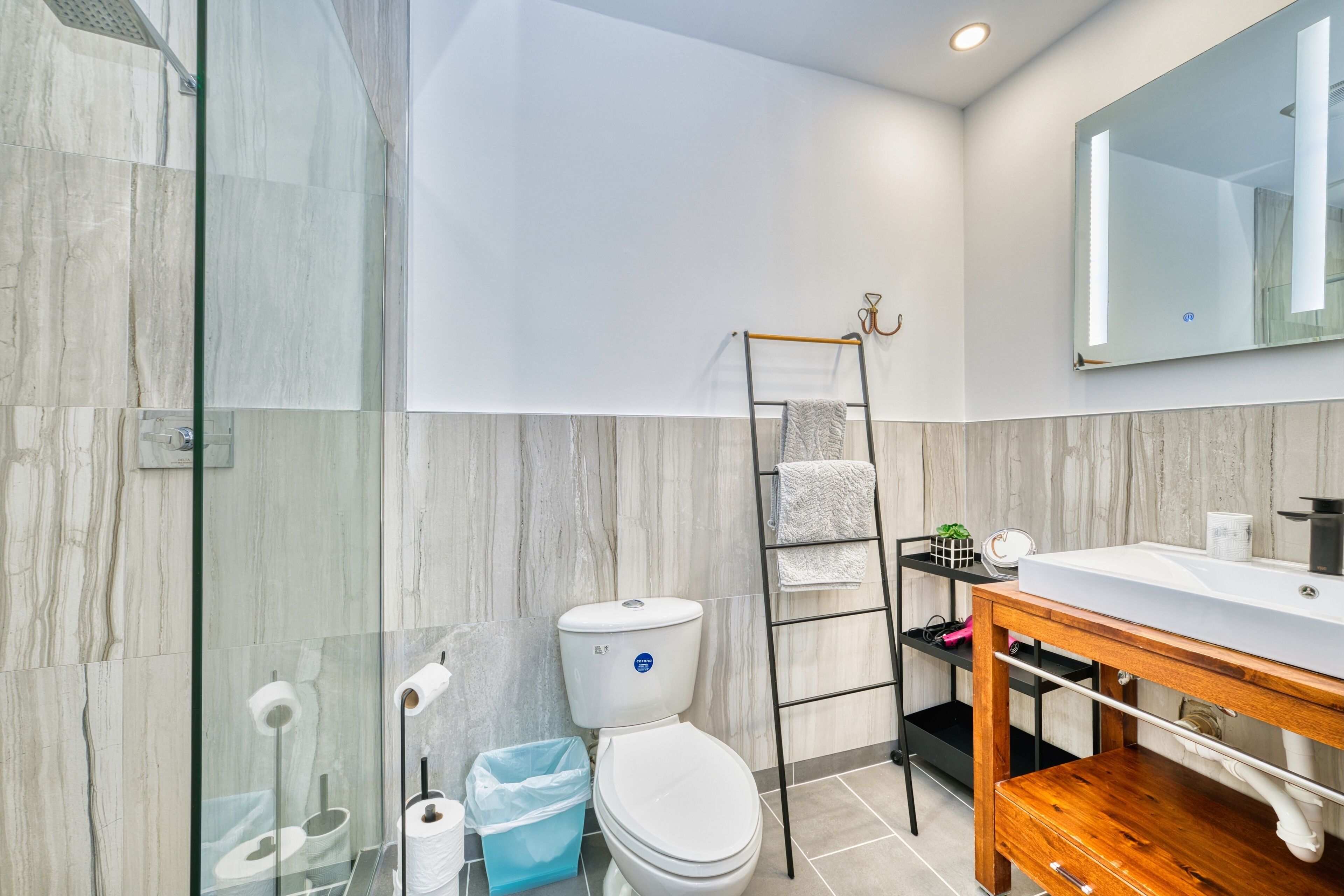 Een moderne badkamer met een douchecabine van glas, een toilet, een wastafel met houten opbergruimte en een spiegel erboven.