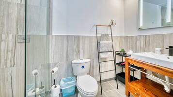 Een moderne badkamer met een douchecabine van glas, een toilet, een wastafel met houten opbergruimte en een spiegel erboven.