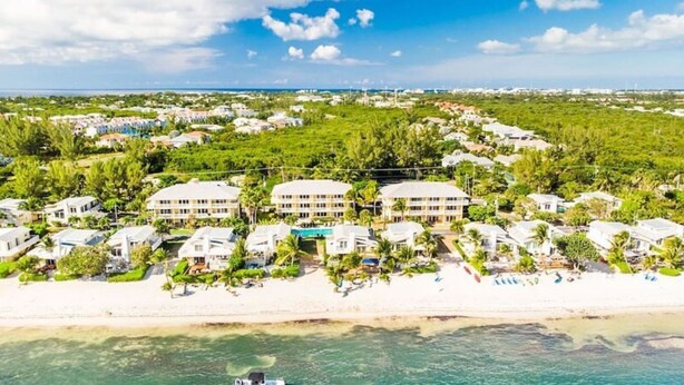 A coastal resort with beachfront villas, clear turquoise waters, and a boat docked on the shore. - Quiet Beach Escape - Caribbean Paradise (South Sound)