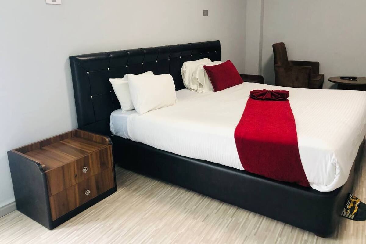 A bed with a black headboard, white bedding, and a red throw. There is a wooden chest of drawers beside the bed.