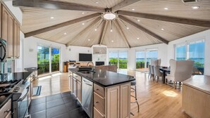 A spacious kitchen with a central island, a dining area with a view, and a large open space with a wooden ceiling.
