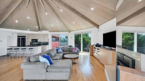 A spacious living area with a large sectional sofa, a kitchen with modern appliances, and a balcony with a view of trees.