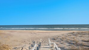 A sandy beach with a wooden walkway leading to the water, under a clear blue sky.