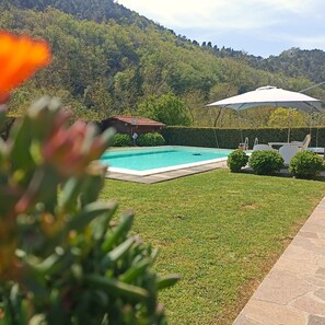 Une piscine dotée d’une terrasse en bois, entourée d’une pelouse bien entretenue et avec une chaîne de montagnes en toile de fond.