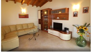 Una sala de estar con sofá, televisor, aparador de madera y un jarrón con flores.