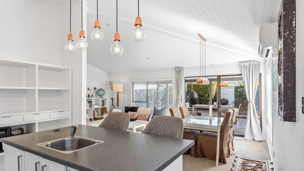 Une cuisine moderne dotée d’un îlot central, d’un coin repas avec une table et des chaises, et offrant une vue sur l’extérieur grâce à de grandes fenêtres.