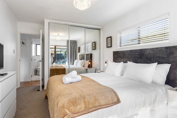 Una habitación de hotel moderna con una cama grande, televisión, armario y baño visible a través de una puerta de cristal.