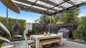 Une terrasse en bois avec une table et des chaises, un fauteuil suspendu et un barbecue.