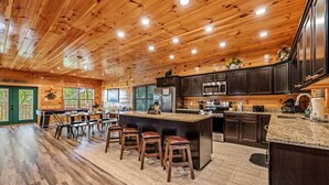 A spacious kitchen with a large island, dark wooden cabinets, and a granite countertop. - 4BR Pool Cabin*Hot Tub*Arcade*Great location! (Sevierville)