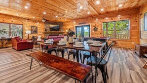 A spacious wooden cabin with a dining area, a living room with a red sofa, and a fireplace. - 4BR Pool Cabin*Hot Tub*Arcade*Great location! (Sevierville)