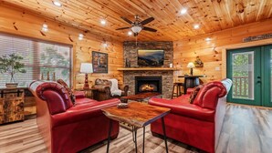 A cozy log cabin interior with a fireplace, leather sofas, and a dining table. - 4BR Pool Cabin*Hot Tub*Arcade*Great location! (Sevierville)