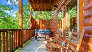 A wooden deck with a hot tub and seating area, surrounded by trees. - 4BR Pool Cabin*Hot Tub*Arcade*Great location! (Sevierville)