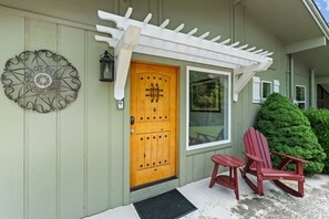 Una casa con puerta de madera, un porche con barandilla blanca y dos sillas Adirondack rojas.