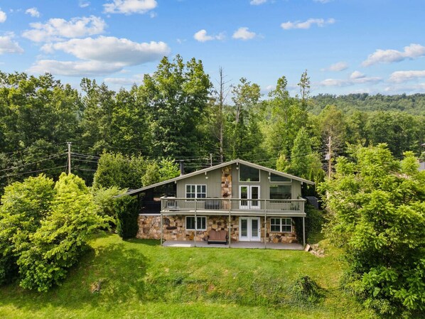 A two-story house with a stone facade, a balcony, and a large front lawn.