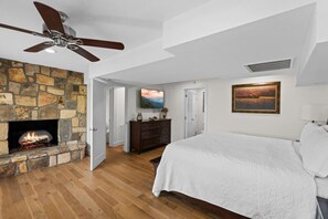 A bedroom with a stone fireplace, a bed, a ceiling fan, and a painting on the wall. - New! Incredible MTN Views! 3BR w/Hot Tub*Quiet! (Sevierville)