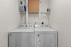 A laundry room with two stacked washers and dryers, a white wall, and a shelf above the dryers.
