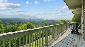 Une terrasse en bois, dotée d’une balustrade, qui offre une vue sur une vallée boisée et des montagnes lointaines.