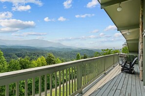 Une terrasse en bois, dotée d’une balustrade, qui offre une vue sur une vallée boisée et des montagnes lointaines.