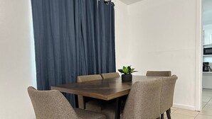 Ein Essbereich mit einem Holztisch und vier gepolsterten Stühlen. Auf dem Tisch steht ein Blumentopf, und dahinter befindet sich ein blauer Vorhang.