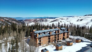 A multi-story building with a flat roof, surrounded by snow-covered mountains and trees. - Pet-Friendly Mountain Studio With Hot Tub, Sauna, and Indoor Heated Pool (Brian Head)