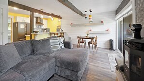 Un salon moderne avec un canapé d’angle, un coin repas avec une table et des chaises, une cuisine équipée d’un réfrigérateur et d’une cuisinière, et une cheminée.