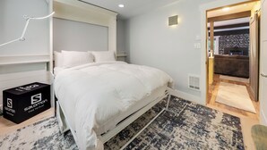 Une chambre à coucher avec un lit, une table de chevet, une lampe, une boîte étiquetée « Il est l’heure de jouer, Salomon » et un tapis à motifs.