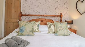 A bedroom with a wooden headboard, floral-patterned pillows, a white bedspread, and a heart-shaped decoration on the wall. - Moot Cottage (Driffield)