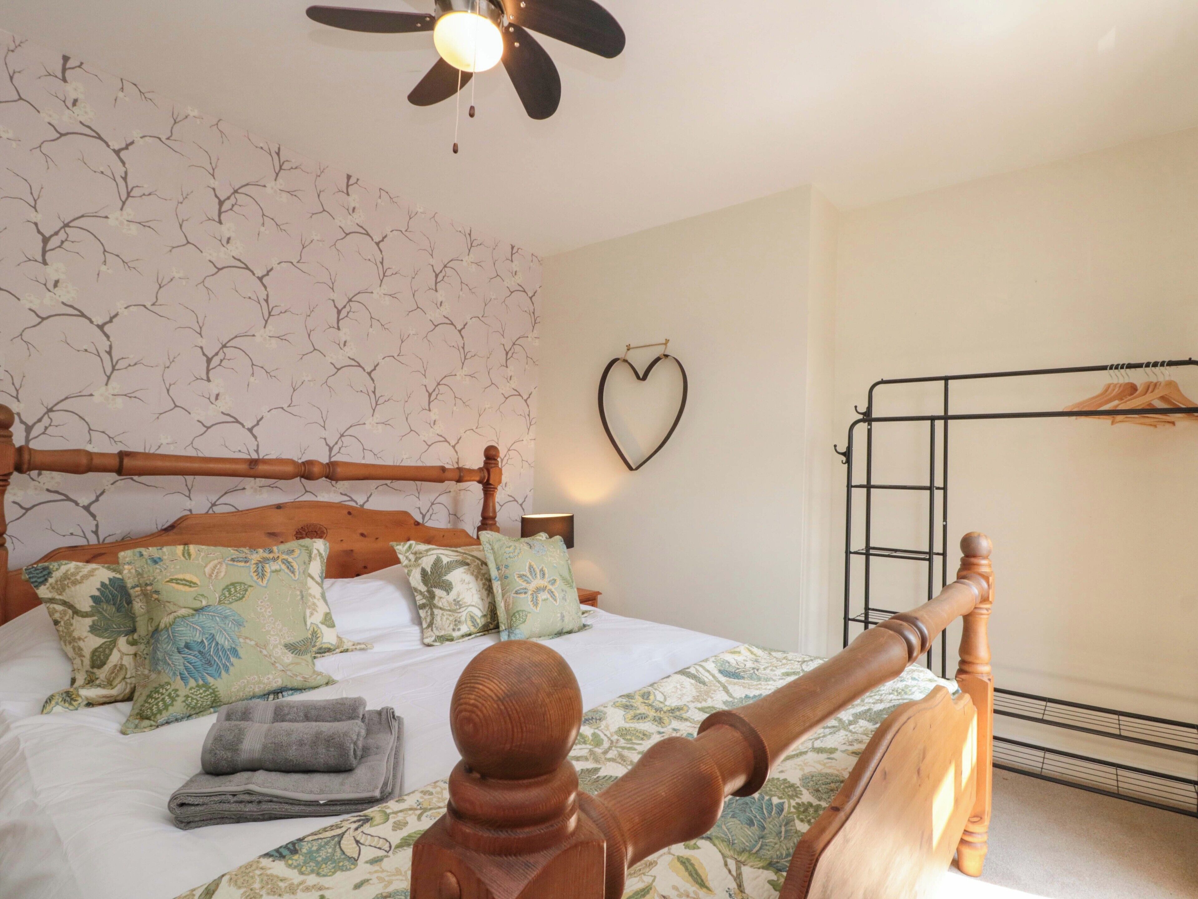 A bedroom with a wooden bed, floral bedspread, and a heart-shaped decoration on the wall.